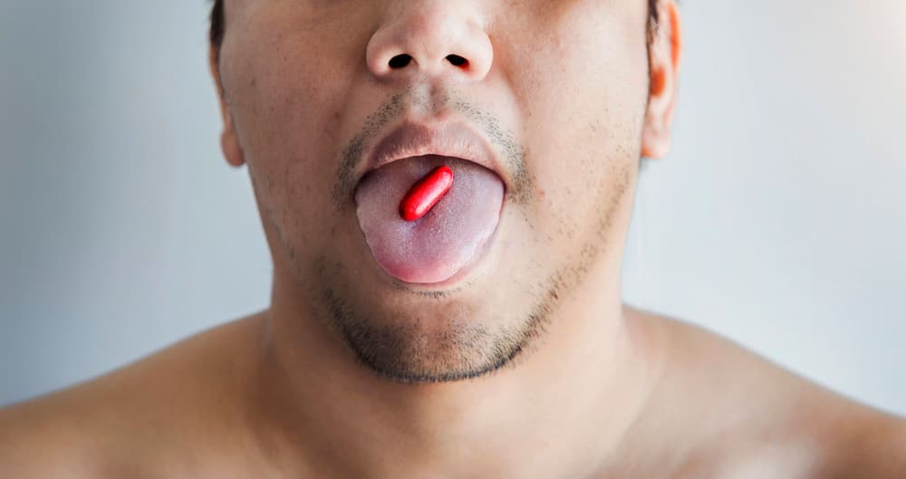 mężczyzna z czerwoną tabletką na języku