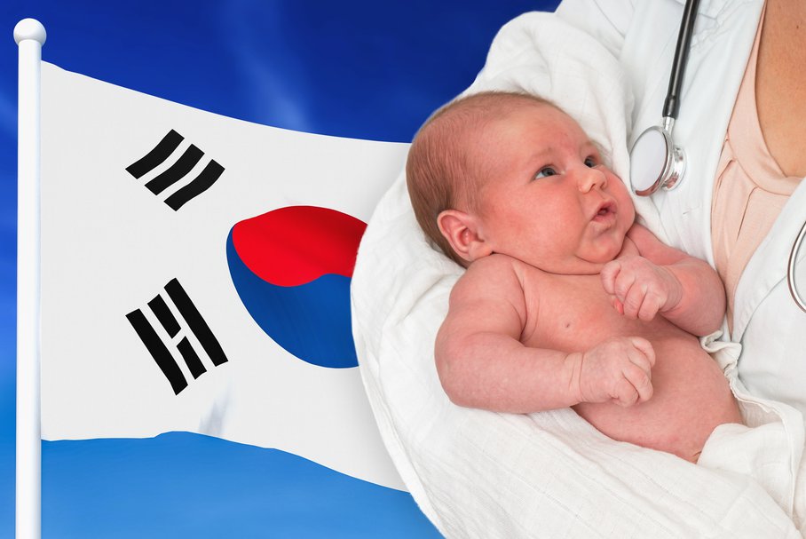 Położna trzymająca noworodka z flagą Korei Południowej w tle.
