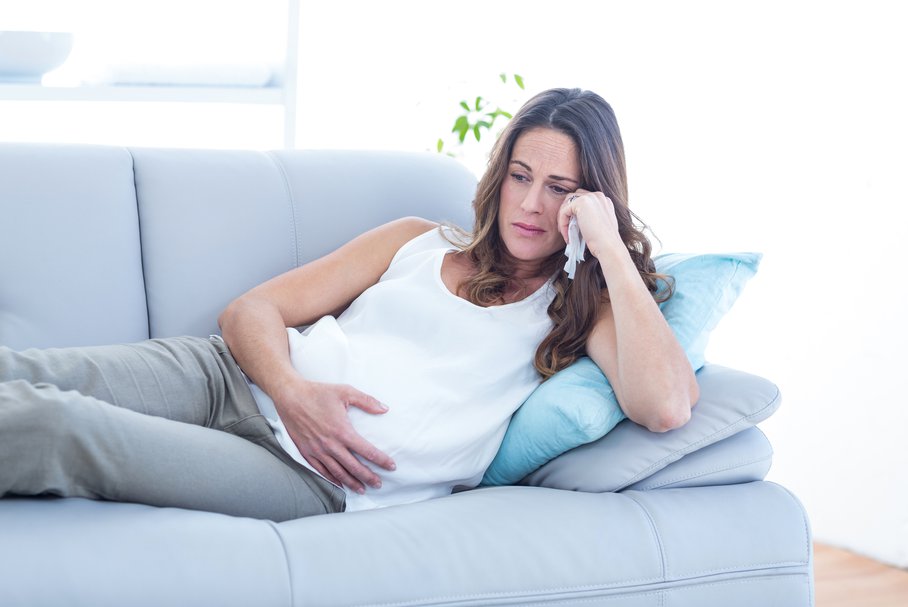 Smutna kobieta w ciąży siedząca na kanapie.