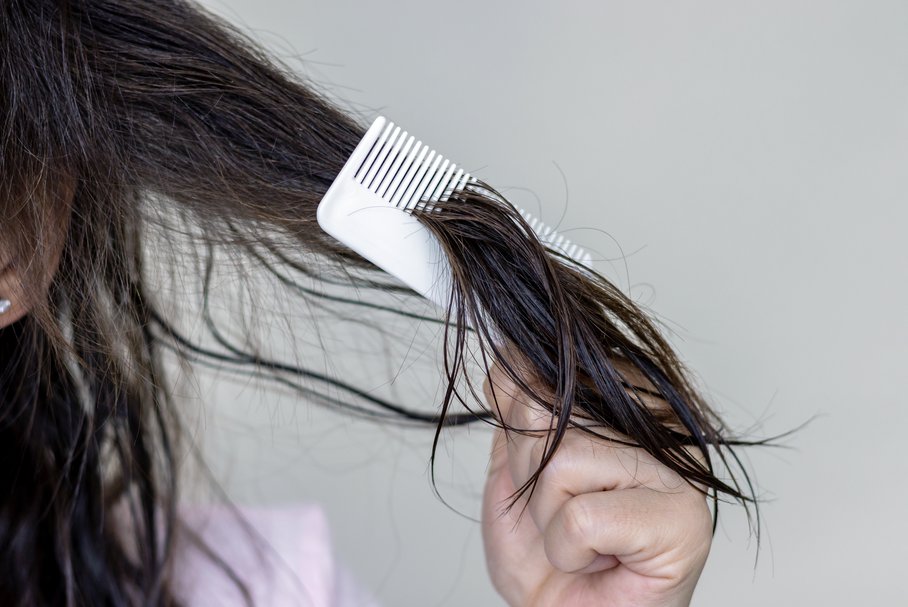 Kobieta rozczesująca grzebieniem zniszczone włosy.